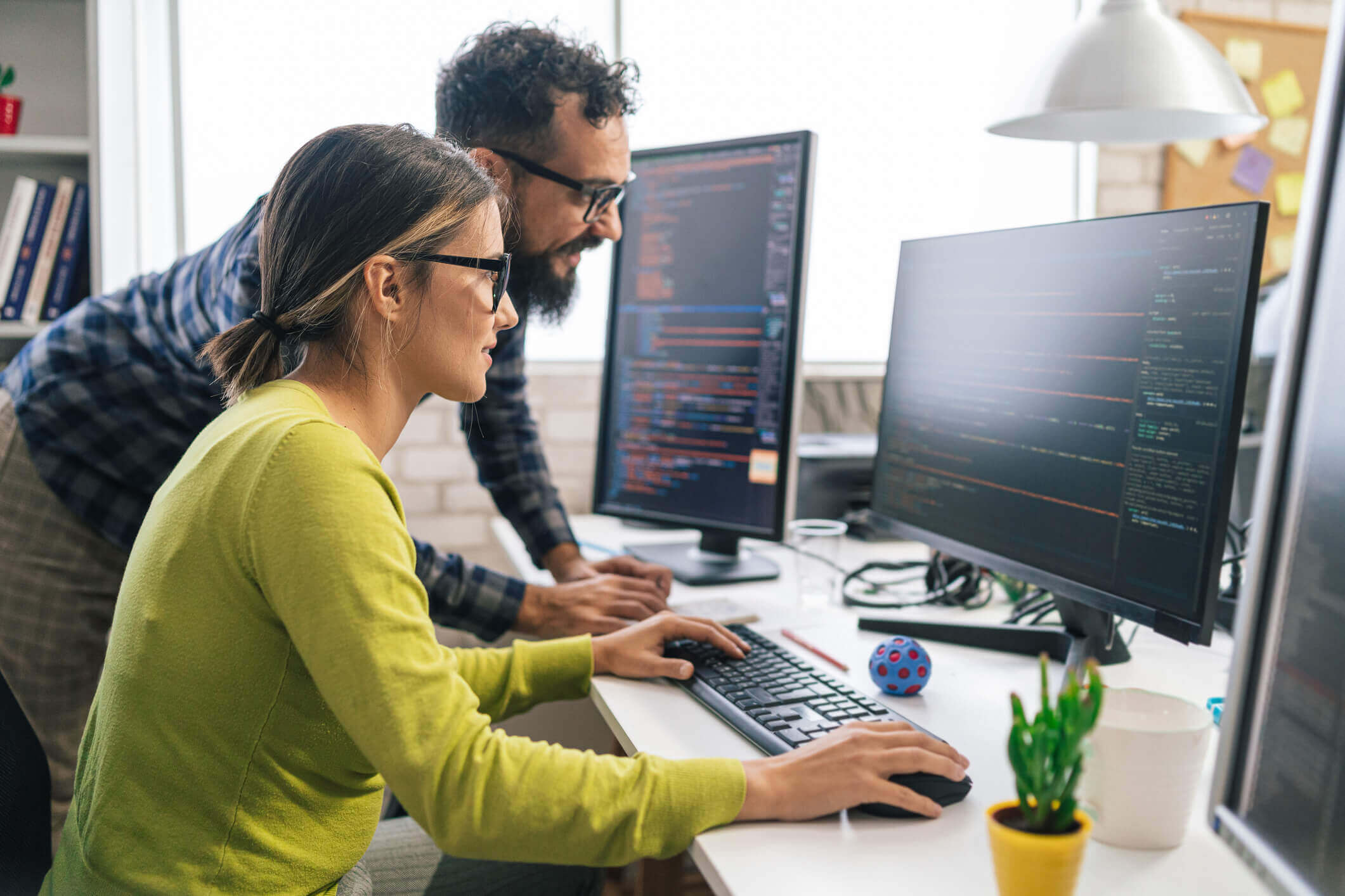 Two people coding on computer screens.